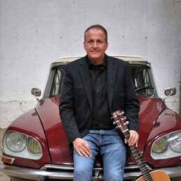 Sänger und Liedermacher Volkwin Müller lehnt mit seiner Gitarre an einem historischen Fahrzeug
