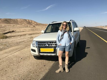 Das Bild zeigt Nicole Albrecht, wie sie auf einer Straße vor einem Geländewagen steht. Im Hintergrund eine Wüstenlandschaft.